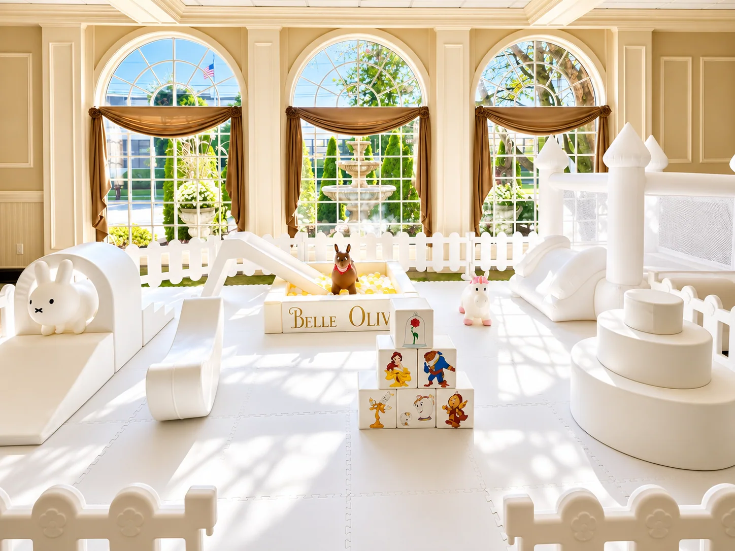 Sunlit deluxe soft play setup with white equipment and a bounce house