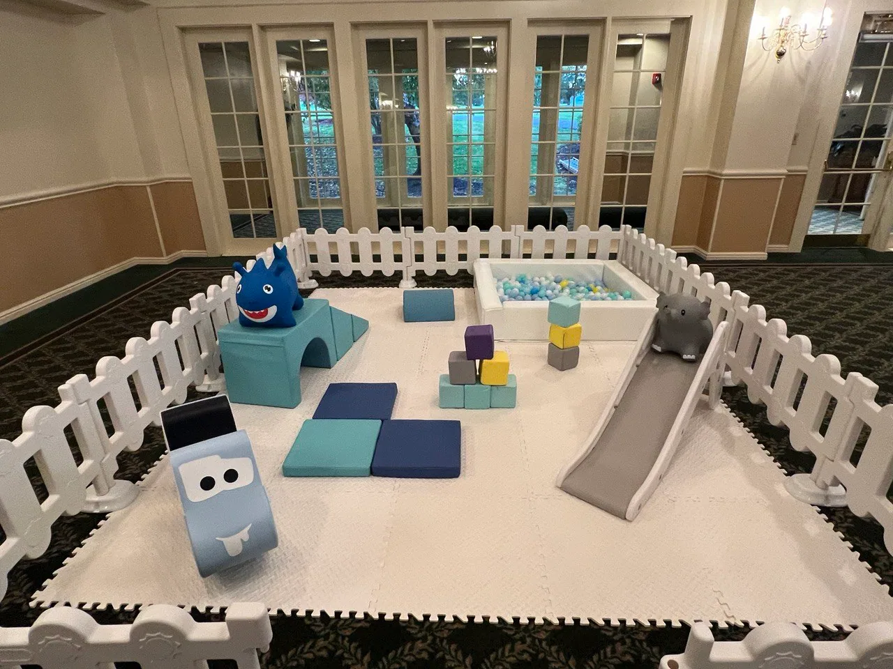 Blue and gray indoor soft play area enclosed by white fencing
